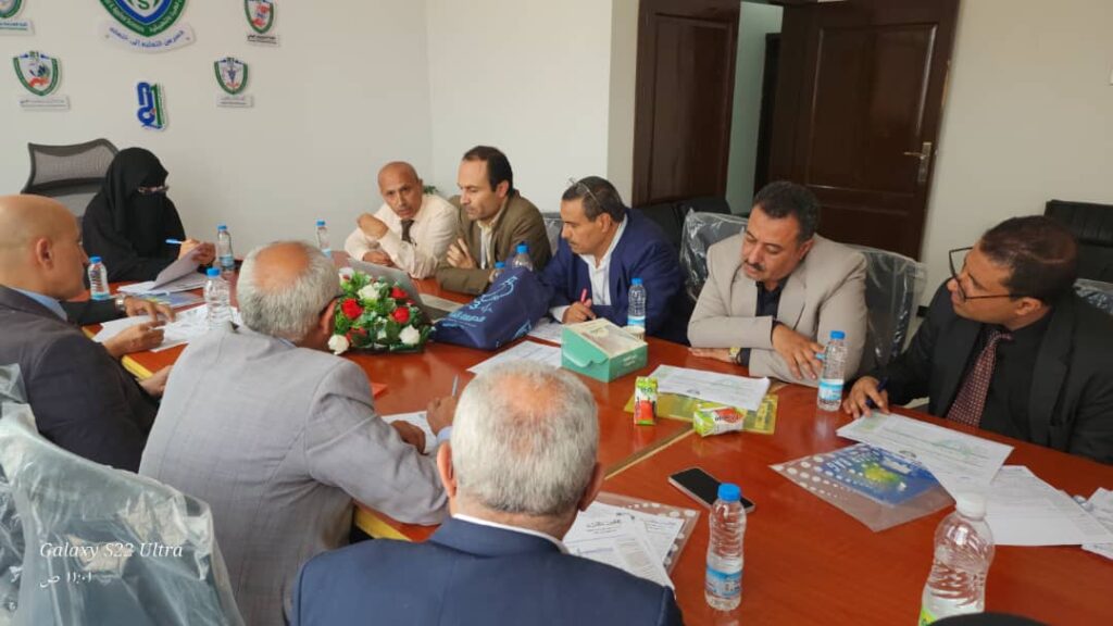 Team of professionals in a meeting around a wooden conference table with documents and water bottles; a flower centerpiece in the middle.