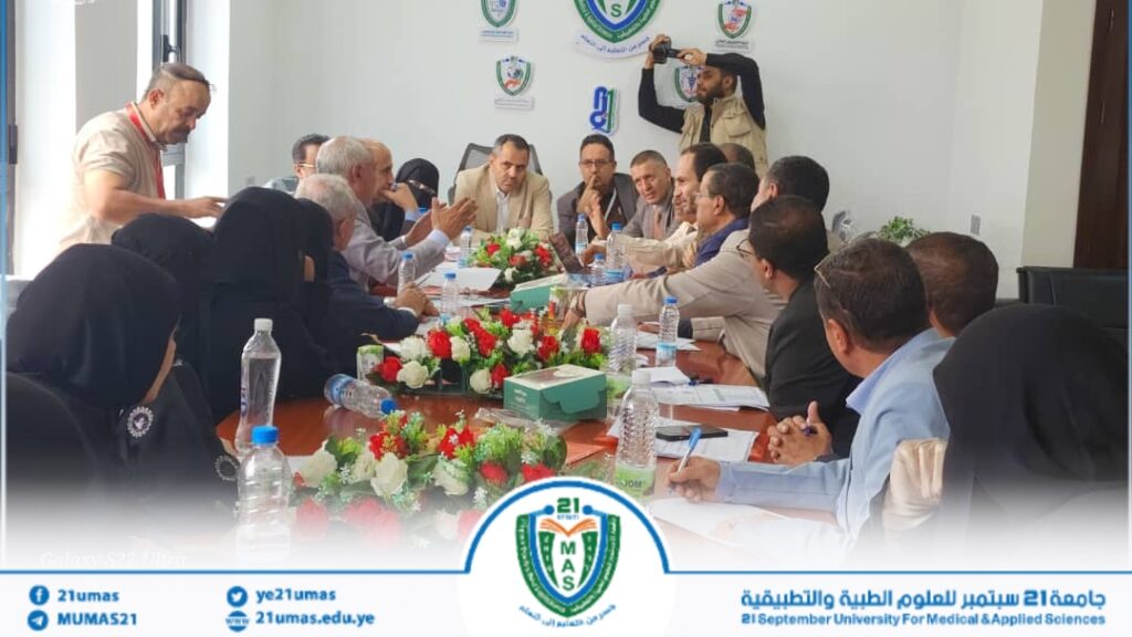 Group of professionals seated around a long conference table, discussing a meeting with floral centerpieces and a photographer in the background.