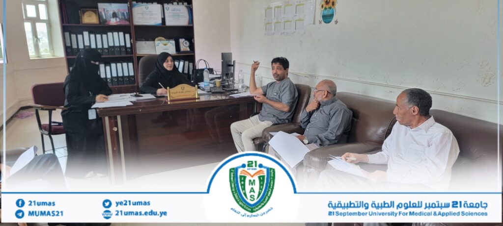 Four people engage in a meeting in a university office: two women in black abayas and two men seated around a desk.