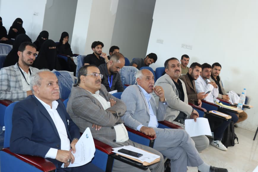 Group of professionals seated in a conference room, some with papers, attentively listening to a presentation at the front.