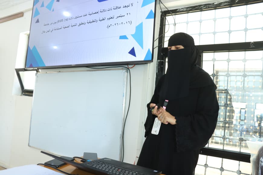 Woman in black abaya and niqab standing beside a presentation screen and whiteboard, holding a projector remote or controller in a classroom setting