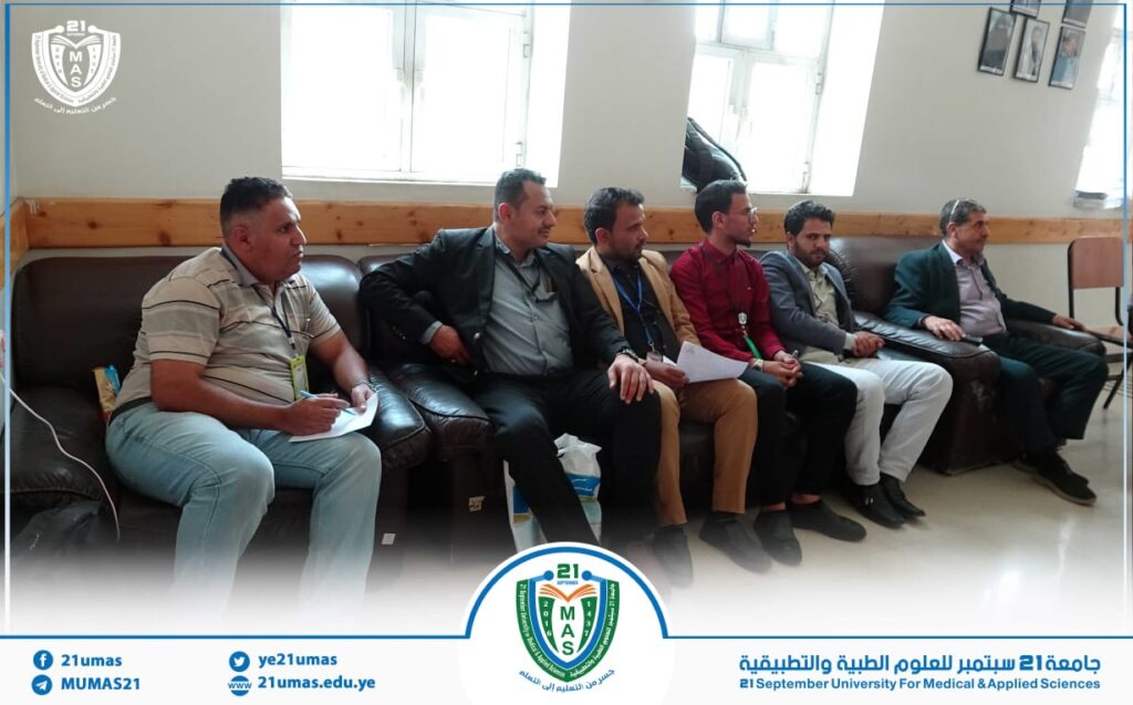 Six men sit on a dark brown leather sofa in a bright room, some holding papers during a university meeting or seminar.