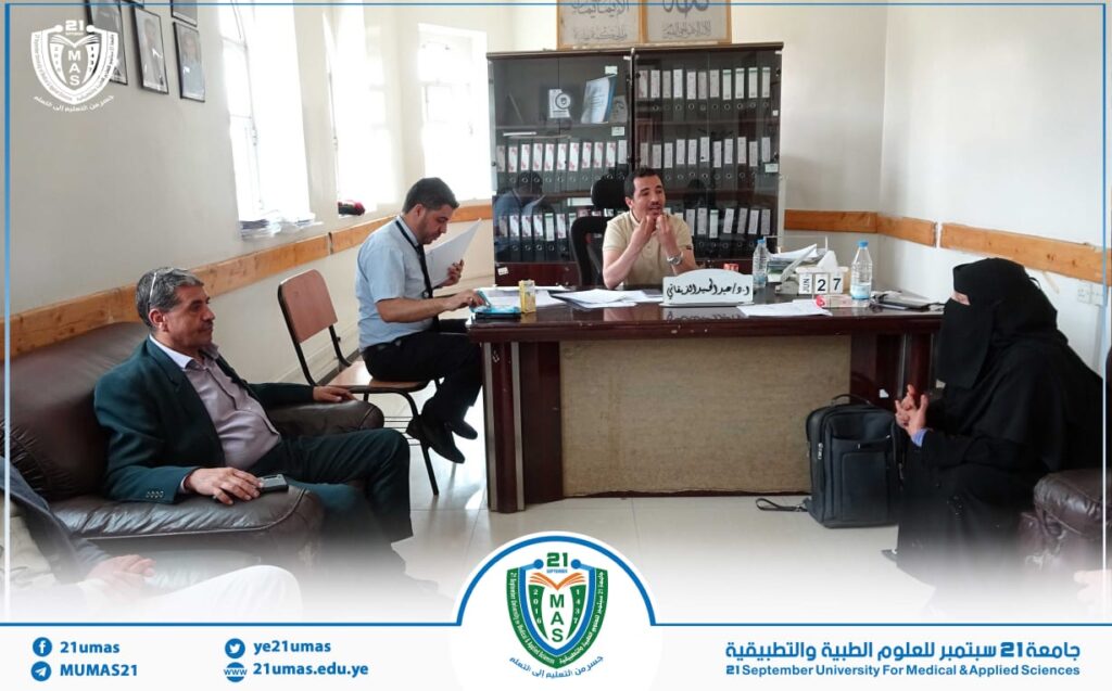 University office meeting: man at the desk speaks while two attendees listen; shelves of binders behind him.
