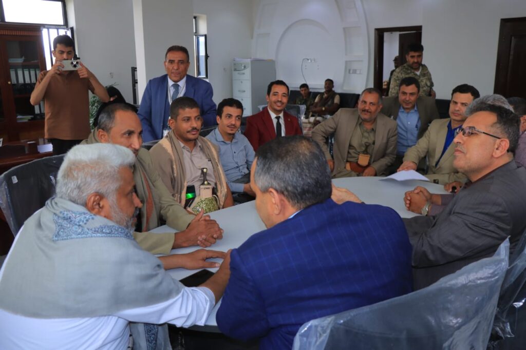 1001114342 - جامعة 21 سبتمبر Group of men in suits gathered around a conference table, hands joined in a show of unity or agreement.