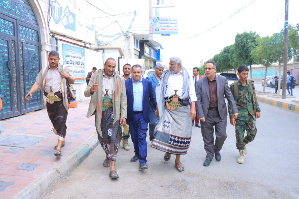 1001114378 - جامعة 21 سبتمبر Group of men walking together on a city street; several wear traditional robes and carry ceremonial jambiya daggers at their waists.