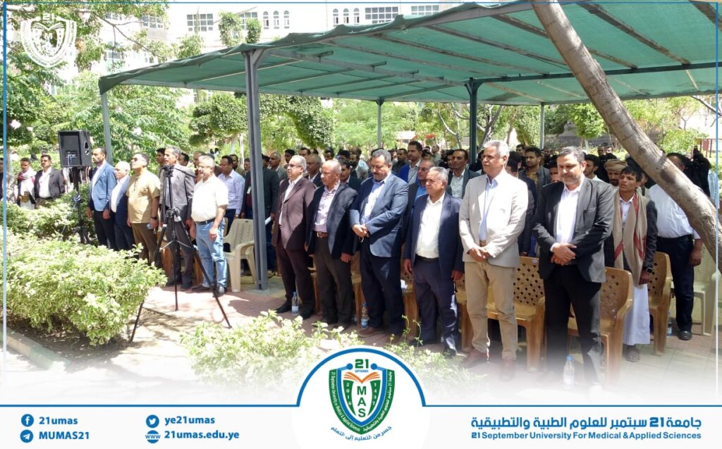 A large group of formally dressed people standing under a green canopy outdoors at a university event.