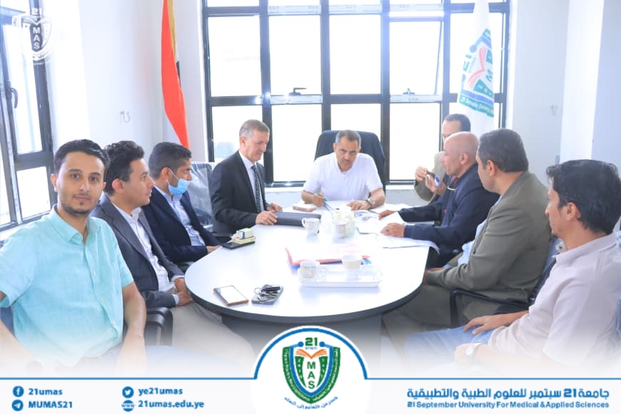 Group of men in business attire seated around a round table in a bright office, engaged in a meeting at a university of medical sciences.