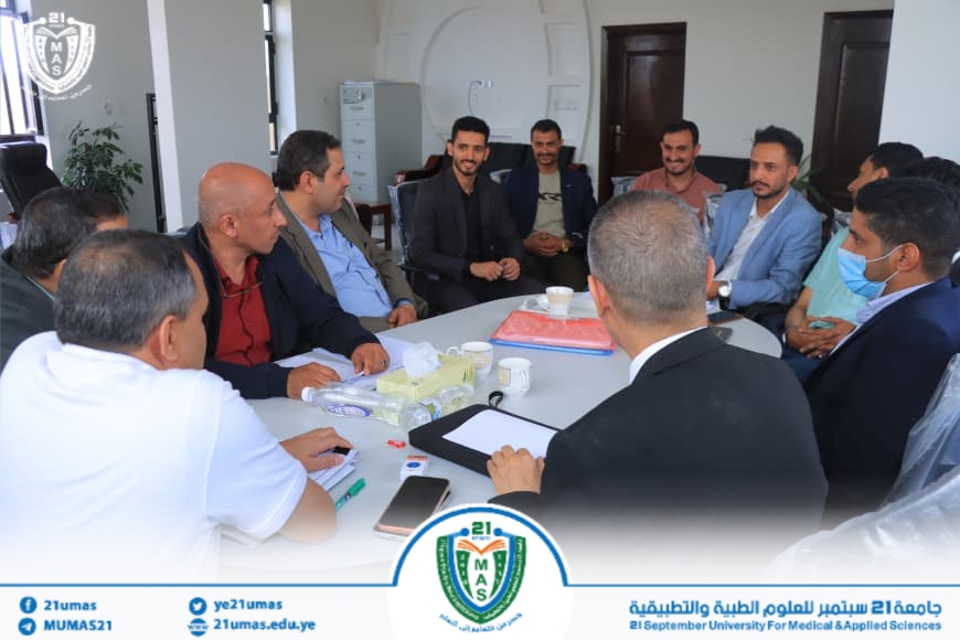 Group of professionals seated around a conference table, discussing in a formal meeting at a dental and medical sciences university center, with cups and documents on the table and a university logo visible.