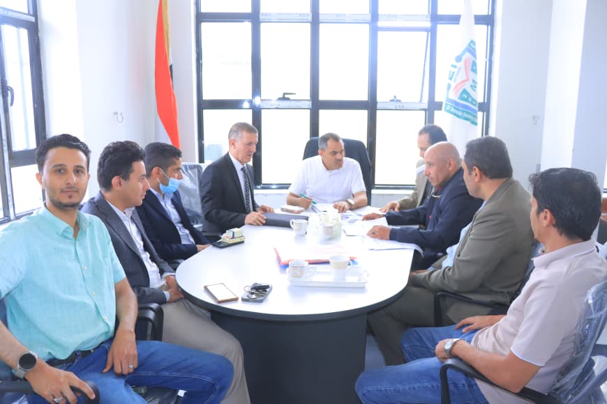 Group of nine men in a business meeting around a round conference table in a bright office.