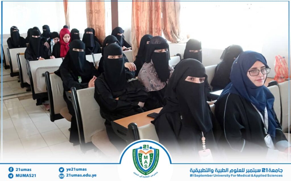 Group of women in hijabs/niqabs seated in a classroom for a university lecture, logo visible at the front bottom edge