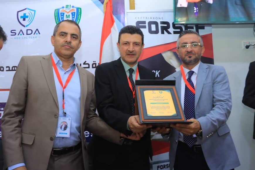 Three men in suits posing with a framed award plaque at a conference session or event behind them.