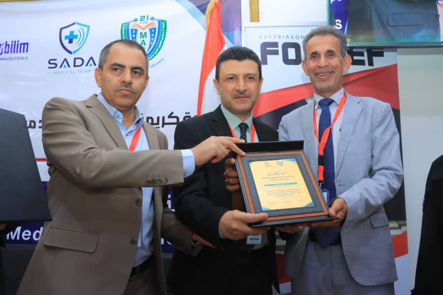 Three men at an award ceremony pose as one presents a framed plaque to another, with smiles and badges around their necks in a conference backdrop.