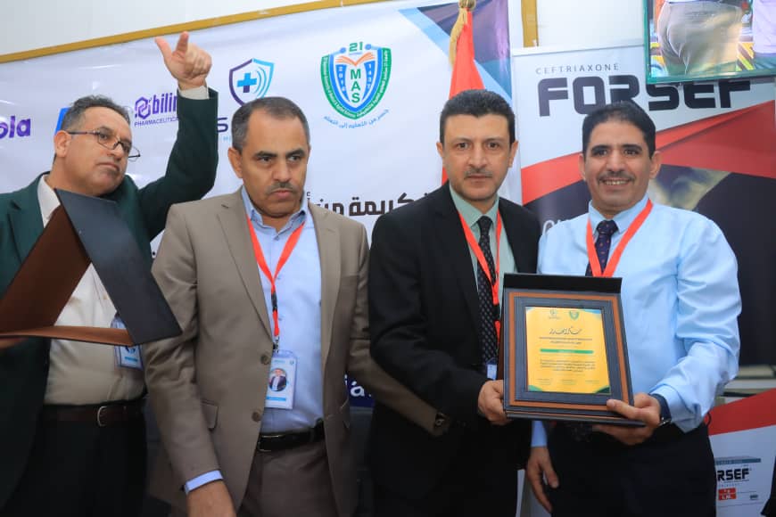Four men in suits posing on a stage after an award ceremony; the man on the far right holds a framed plaque.