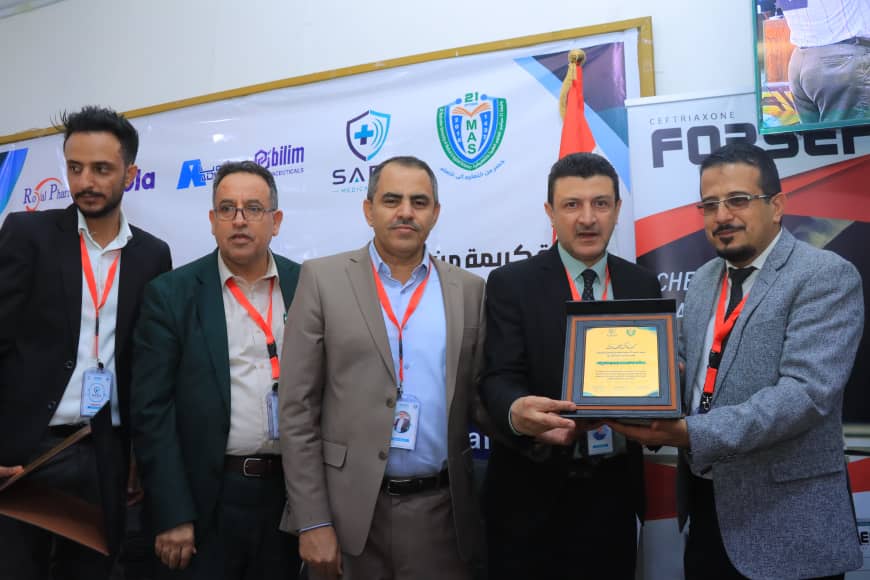 Group of formally dressed men at an awards ceremony; one is presenting a plaque to another while others pose behind them.