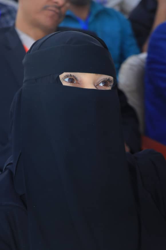 Woman in a black niqab with only her eyes visible, in a crowd behind her.