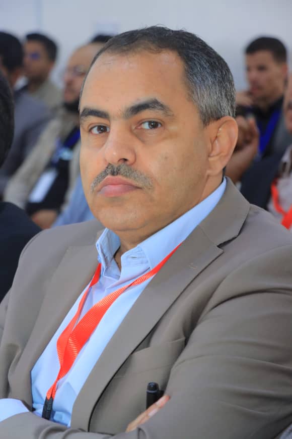 Portrait of a middle-aged man in a beige suit with a red lanyard at a conference session