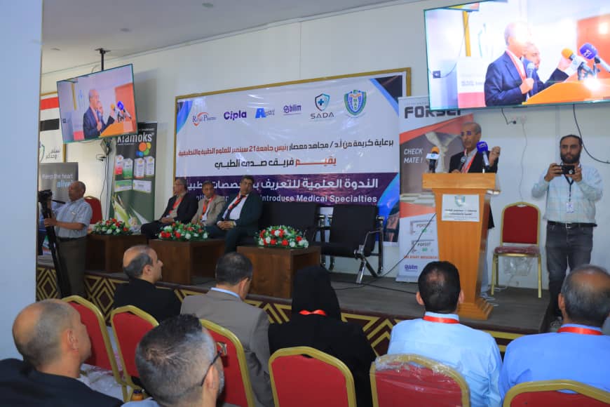 Panel discussion at a medical conference with five men seated on stage and a banner behind them.