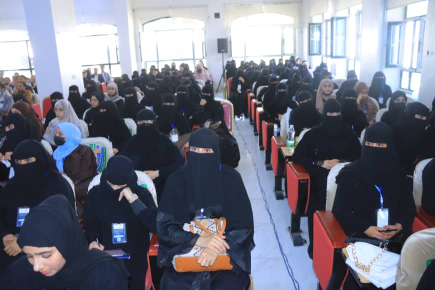 Crowded lecture hall filled with women wearing black niqabs seated in red chairs at a conference room.