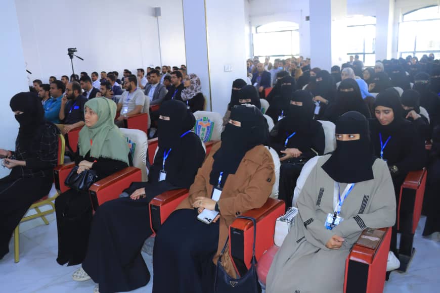 Audience seated in a conference hall, many women wearing black niqab or hijab in the front rows, with attendees in the background.]