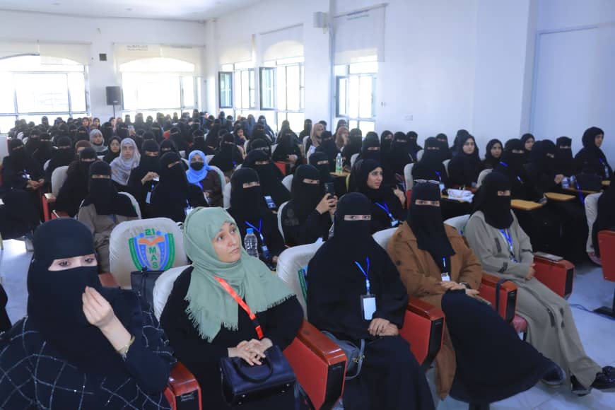 A large group of women in hijabs seated in a bright classroom, attending a seminar with lanyards.