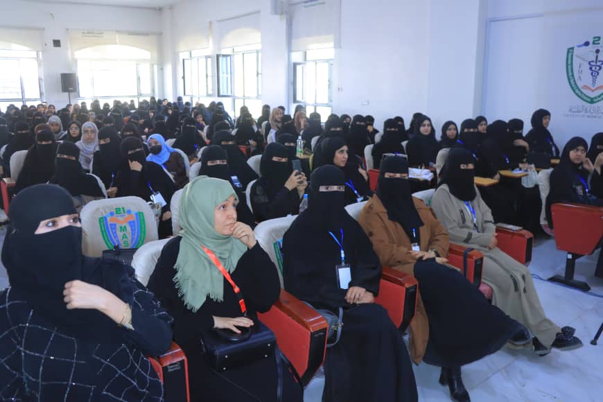 Large hall filled with women in hijabs and niqabs seated in red and white chairs at a conference or seminar edge of the room.