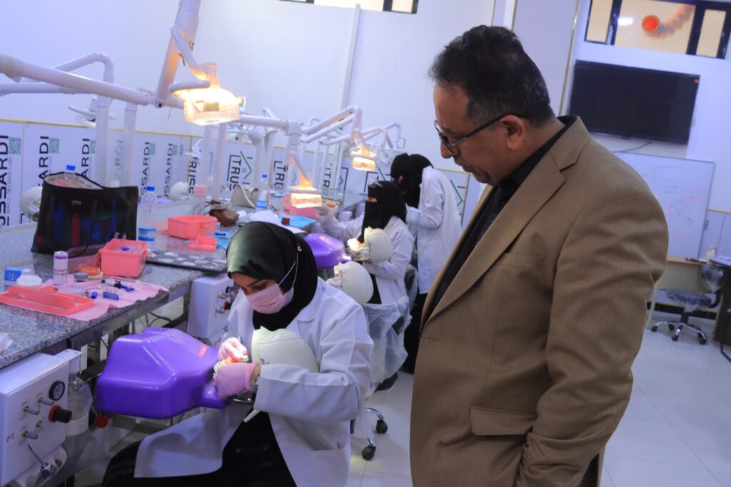 Dental lab scene with technicians in white coats and masks working on dental models under bright lamps, supervisor in a brown suit observing nearby.