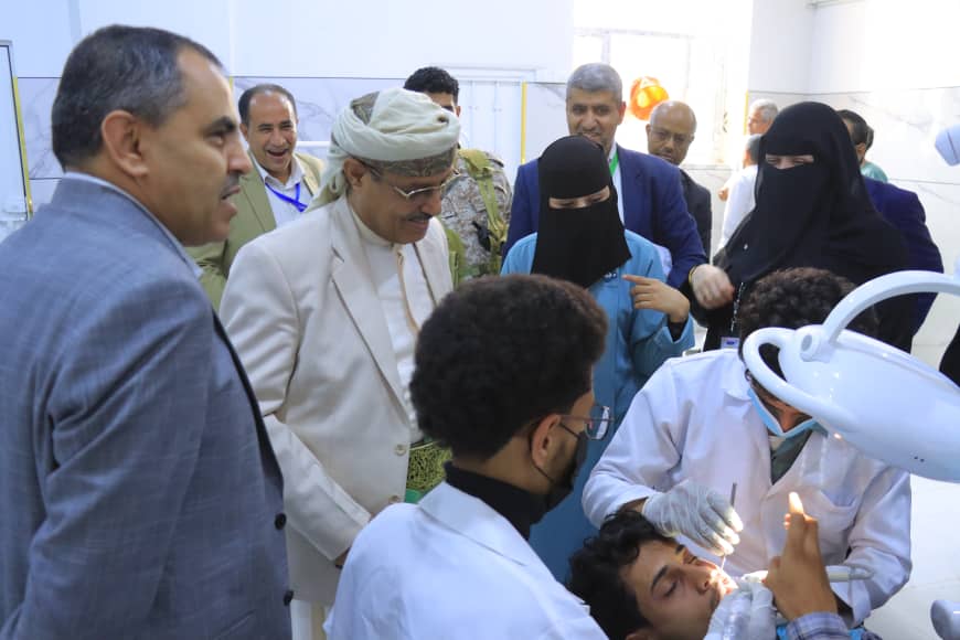 Dentist and assistant perform a dental procedure on a patient while a group of observers watches in a clinic.