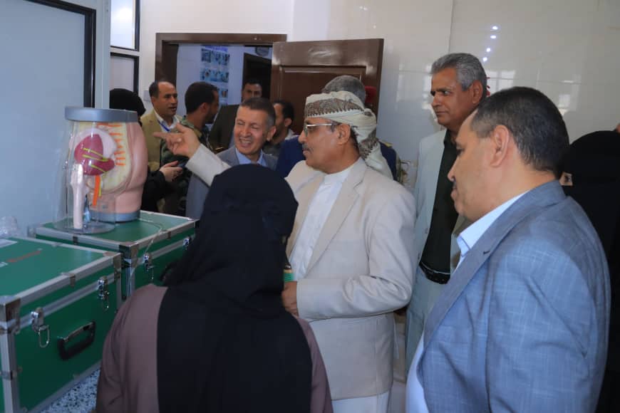 Officials in a medical facility watch a doctor or guide point to a transparent display case containing a heart model.