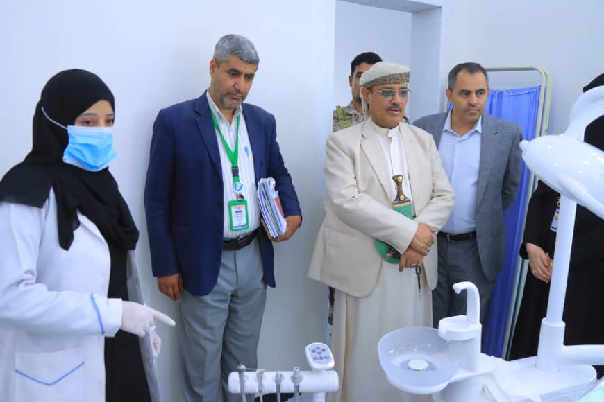 Group of professionals in a clinic examining a dental chair and equipment; a nurse in a white coat and mask stands nearby.