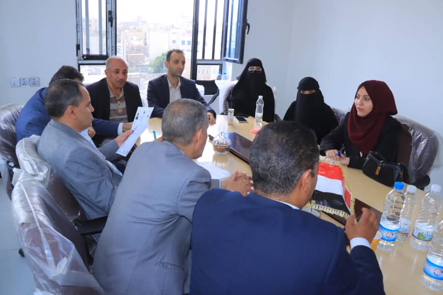 Group of professionals around a conference table in a bright room, several wearing hijabs, discussing documents.