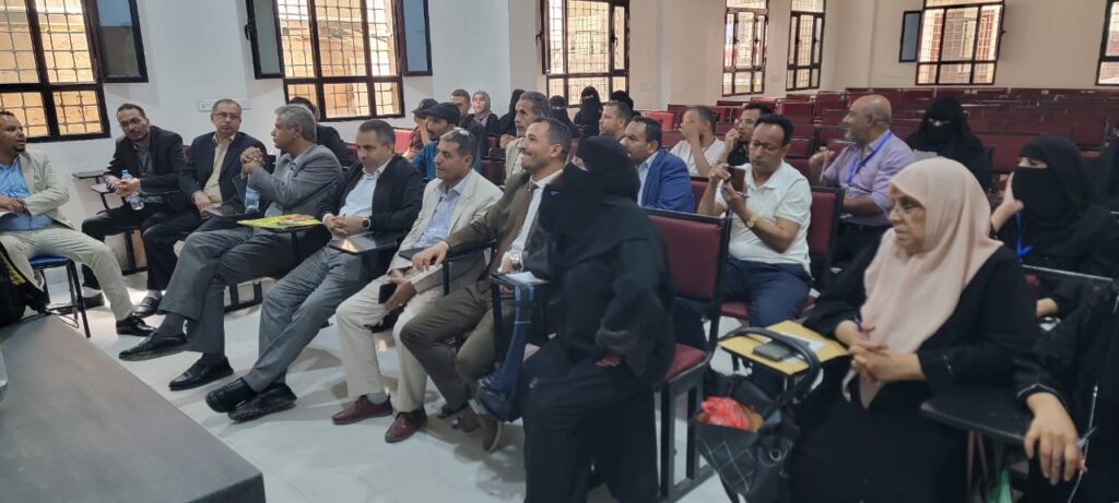 Group of formally dressed attendees seated in a conference room, listening to a presentation.