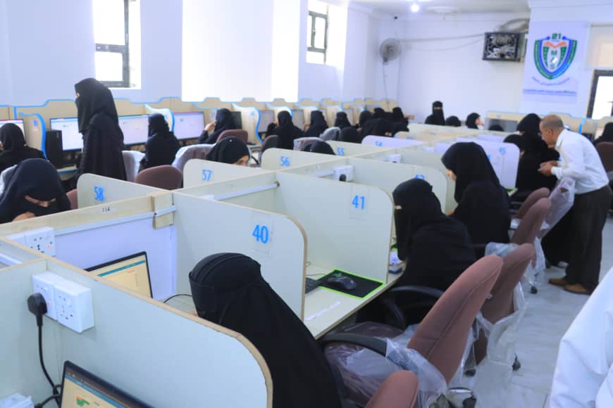 A large computer lab with rows of cubicles and people wearing black abayas working at desktop computers.