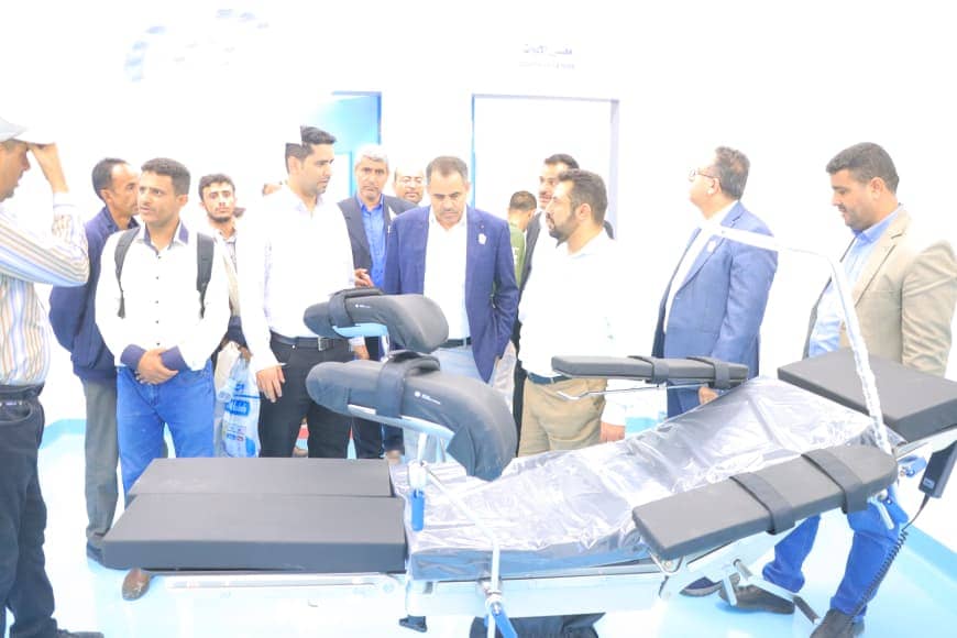 Group of men in business attire gathered around a hospital stretcher on display in a bright showroom.