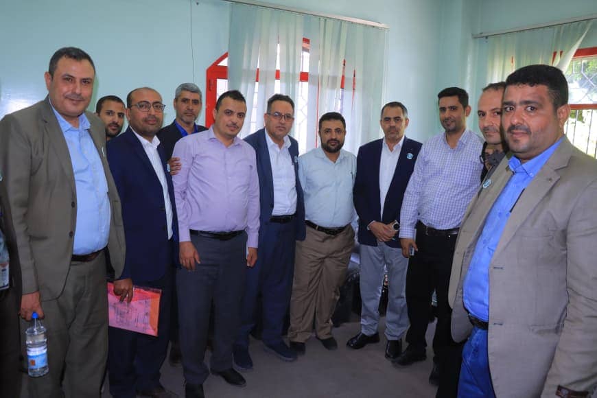 Group of men in business attire posing for a group photo indoors, suggesting a formal meeting or event.