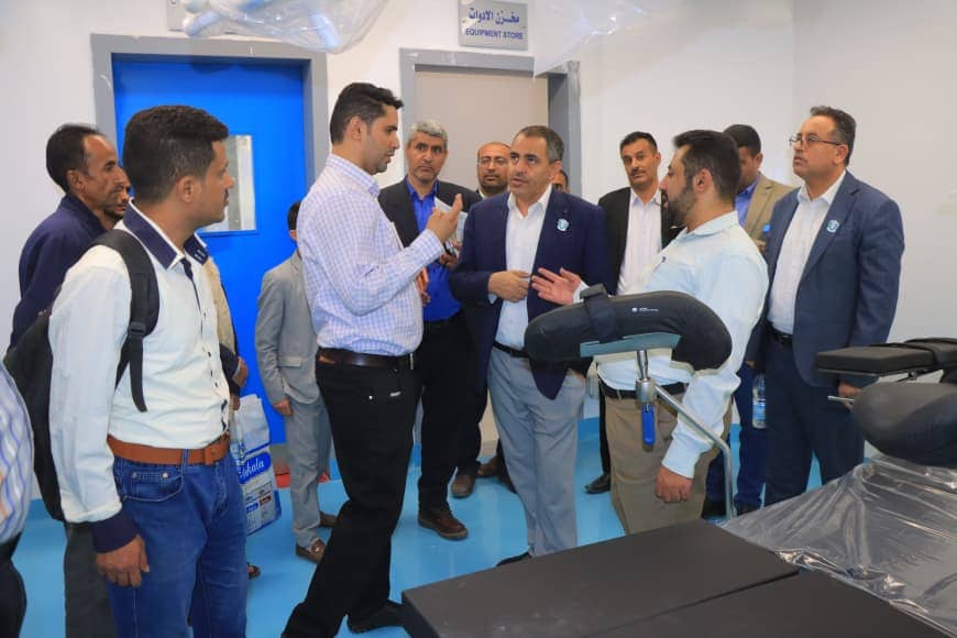 Group of men in business attire standing in a medical equipment showroom, discussing near a dental chair in the foreground.