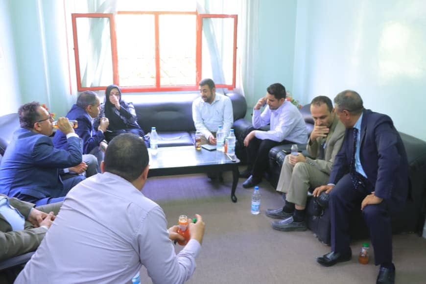 Group of professionals seated in a circle in a bright room, sharing drinks during a casual meeting around a coffee table with bottles and cups on it.