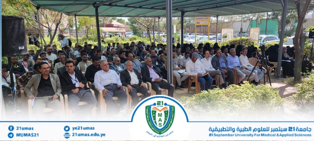 Audience seated under a tent at an outdoor university event, with a banner and logo for 21 September University for Medical & Applied Sciences in the foreground.
