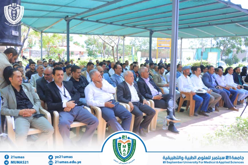 Row of men in business attire seated outdoors under a teal canopy at a university event.] , Row of men in business attire seated outdoors under a teal canopy at a university event.