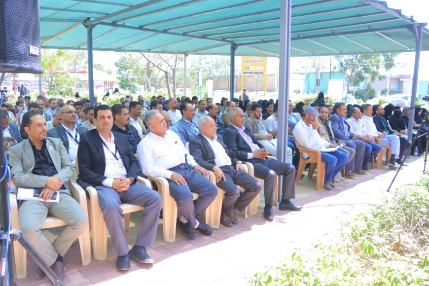 A large group of people seated in rows under a turquoise canopy at an outdoor event or conference.
