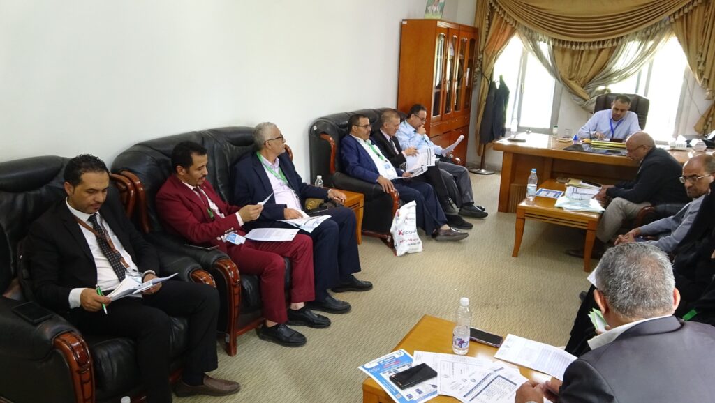 Group of men in suits seated on leather couches reviewing documents during a formal meeting in an office.