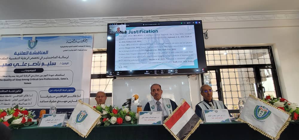 Three doctors sit at a panel desk during a medical conference, with banners, flower garlands, and a screen displaying a slide titled'Justification' behind them.