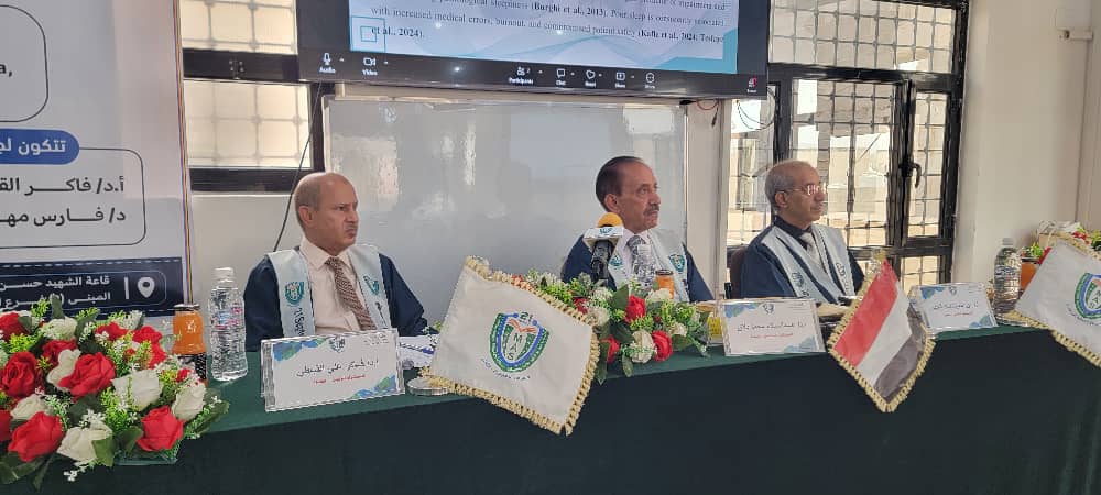Panel of three men in suits at a conference table with flags and flower arrangements, presenting a formal discussion.