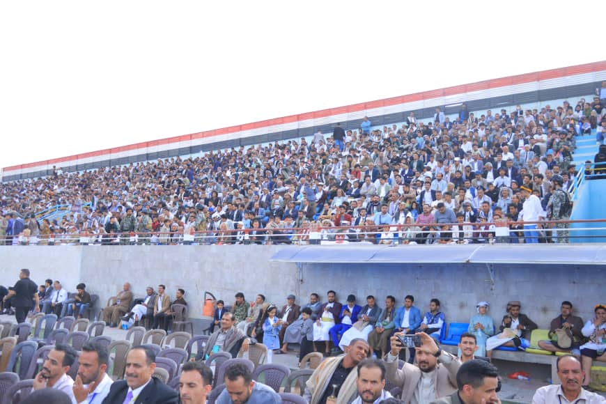 1003982604 - جامعة 21 سبتمبر Large crowd seated in stadium stands during an event at an outdoor venue.