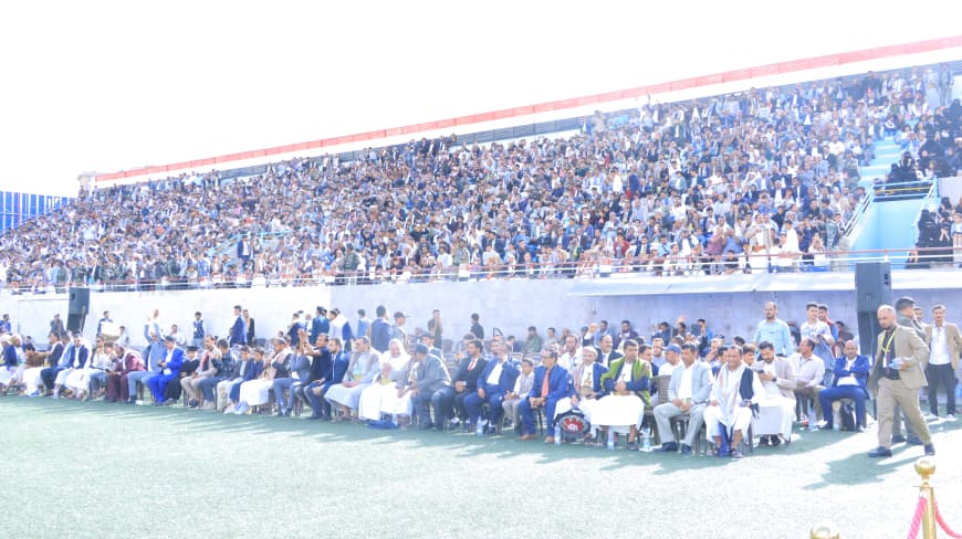 1003984226 - جامعة 21 سبتمبر Large crowd seated in stands and on the field at a stadium during a formal event.