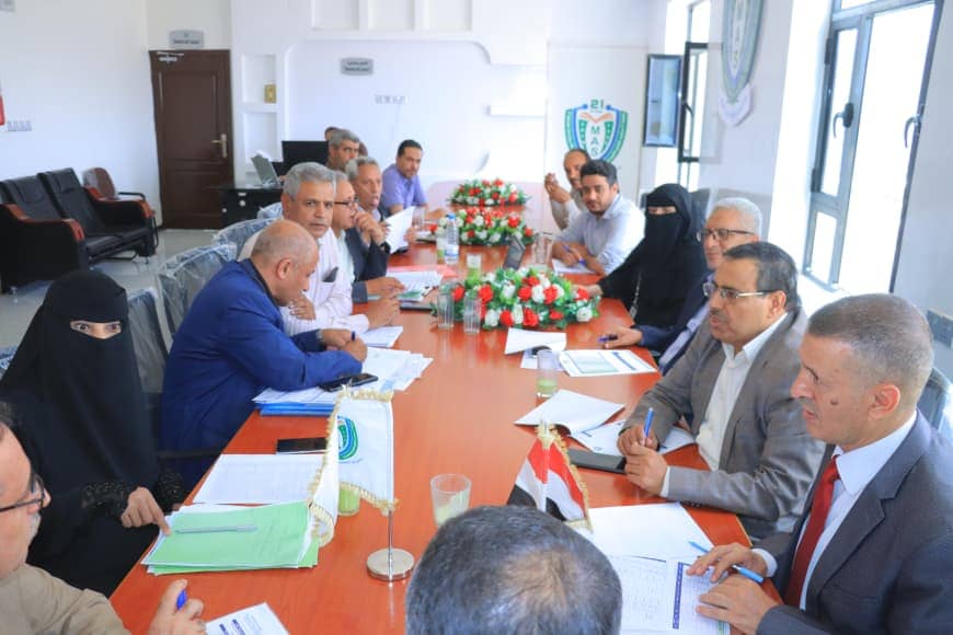 Group of people seated around a long conference table in a bright room, reviewing documents during a formal meeting.
