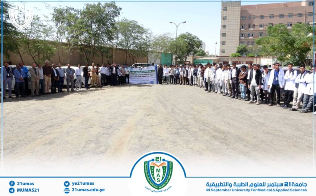 Group of students and staff forming a long arc outdoors for a campus event, banner in the background and university logo at bottom center.