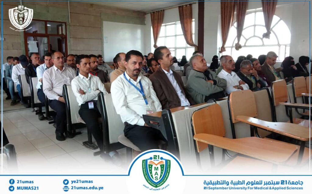 Group of attendees seated in a university lecture hall, listening to a presentation, with a blue-and-white event banner and logo at the bottom.