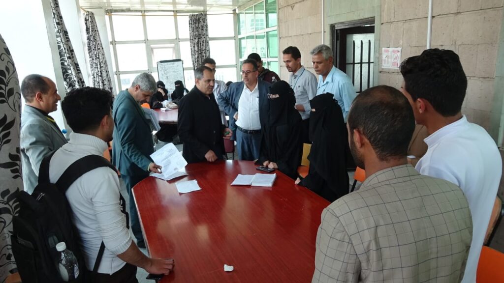Group of people around a red conference table reviewing documents in a bright meeting room.