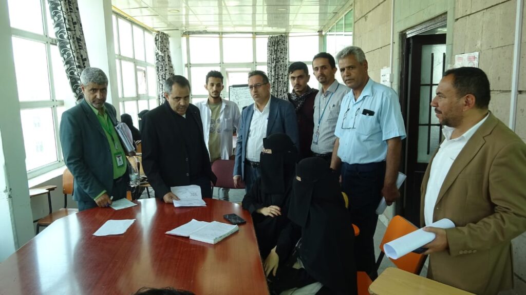 Group of professionals gathered around a conference table reviewing documents in a bright room, with two women in niqab seated at the table.