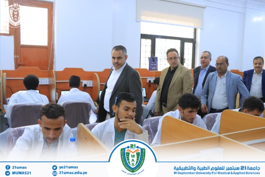 Group of men in suits observing students in white lab coats working at desks in a medical university lab.